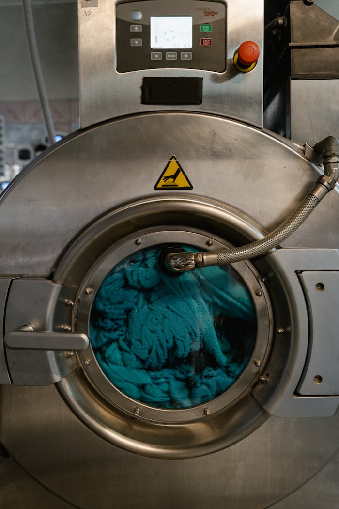 Close-up view of an industrial washing machine with blue fabric during a wash cycle in a laundromat.