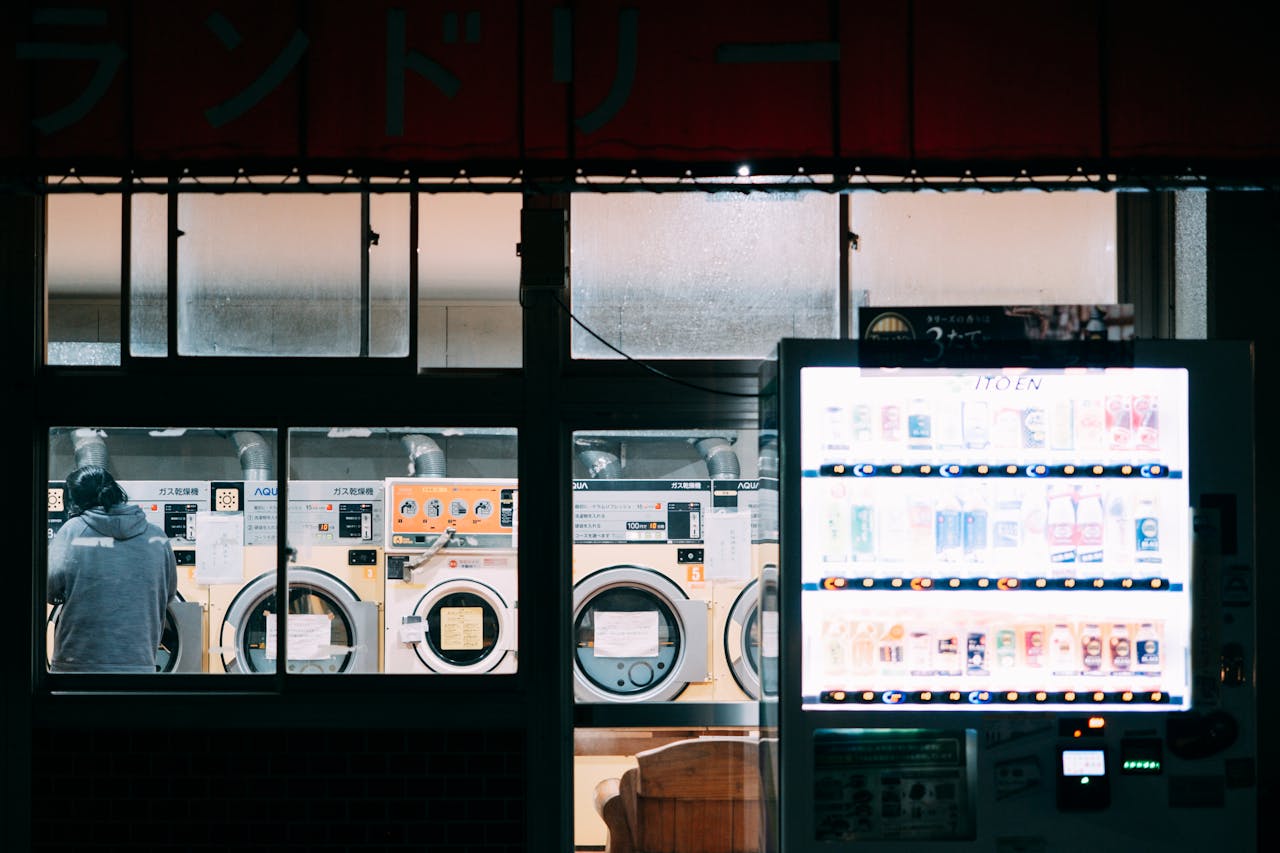 A cozy nighttime scene at a laundry shop with a bright vending machine and washing machines.
